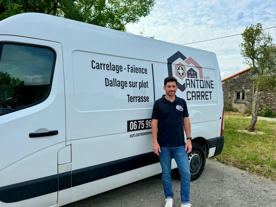 Artisan carreleur posant devant sa camionnette de travail blanche, en extérieur, tenue polo bleu marine
