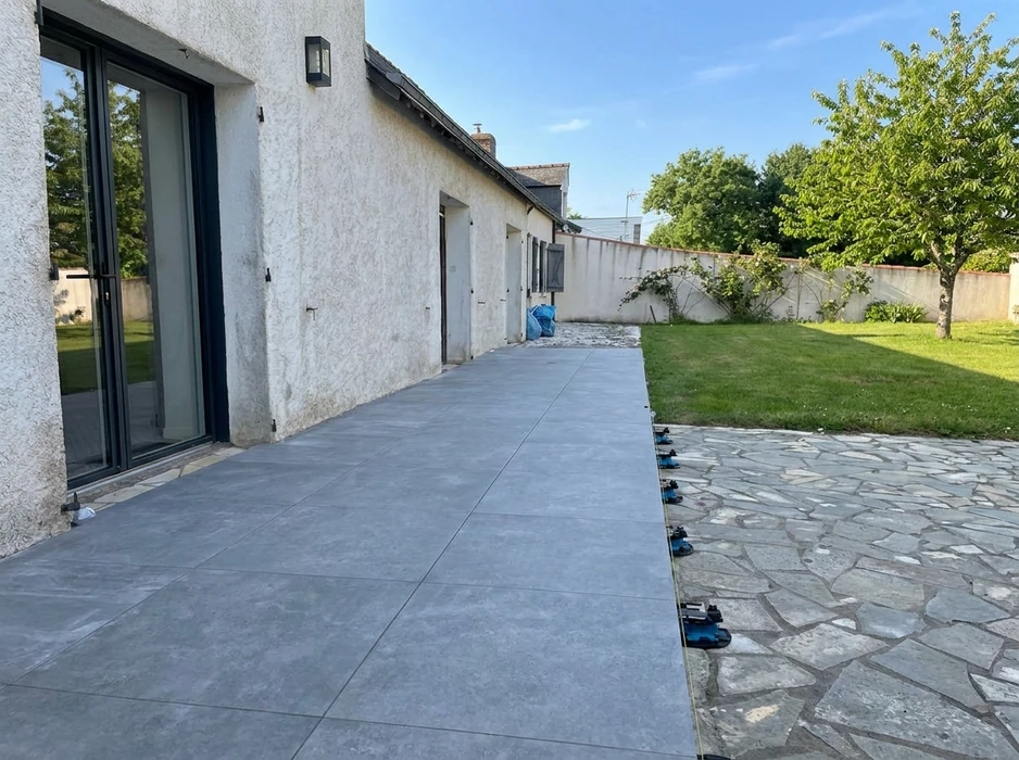 Terrasse extérieure longeant une maison en enduit blanc, en cours de pose