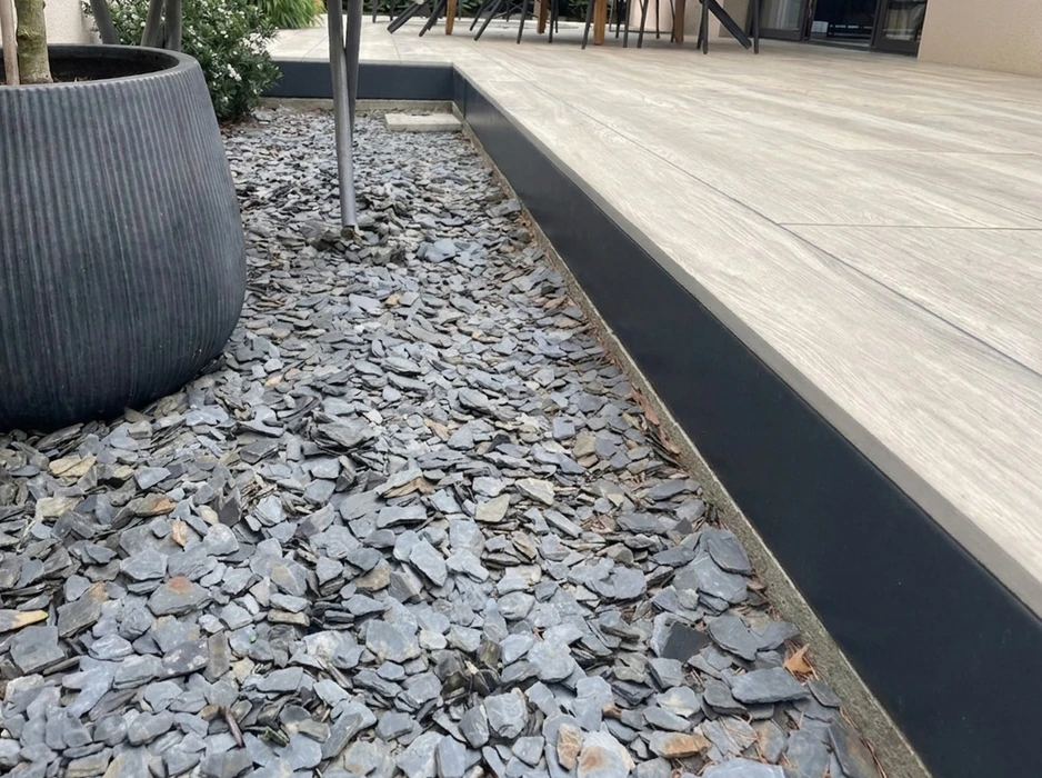 Aménagement extérieur contemporain : terrasse en composite imitation bois gris clair, bordée d'un profil de finition aluminium anthracite