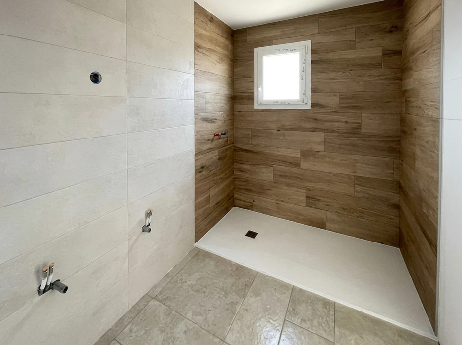 Douche à l'italienne en cours de finition, carrelage mural hexagonal blanc avec motifs décoratifs noirs et effet bois 3D disposés aléatoirement