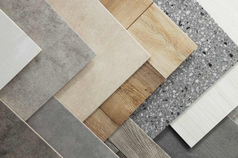 Un artisan carreleur en vêtements de travail blancs applique de la colle à carrelage sur un mur intérieur à l'aide d'une spatule crantée