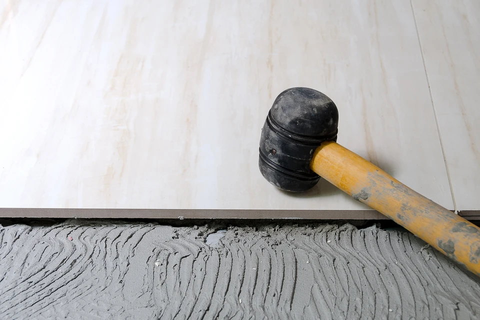 Ouvrier carreleur en tenue de travail applique de l'adhésif sur carrelage blanc avec spatule crantée