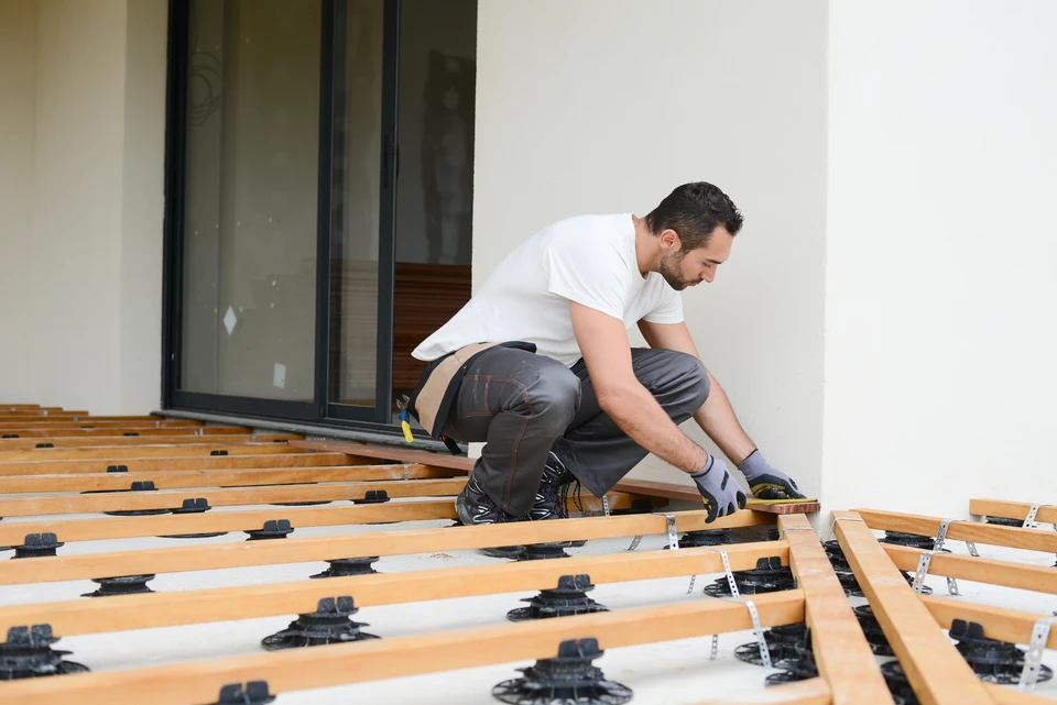 Ouvrier en équipement de protection installant un dallage extérieur, utilisant un marteau à tête jaune pour ajuster les pavés sur lit de sable