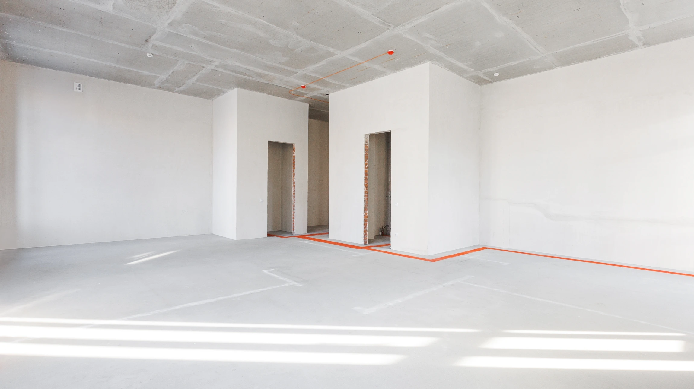 Ouvrier en salopette et casque orange utilise une lisseuse électrique sur chape béton dans pièce en rénovation